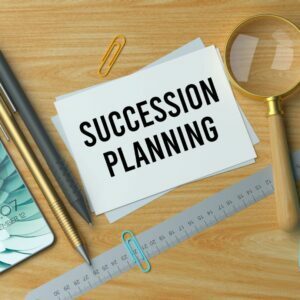 succession planning written on a card on a desk next to a ruler, magnifying glass and pens.